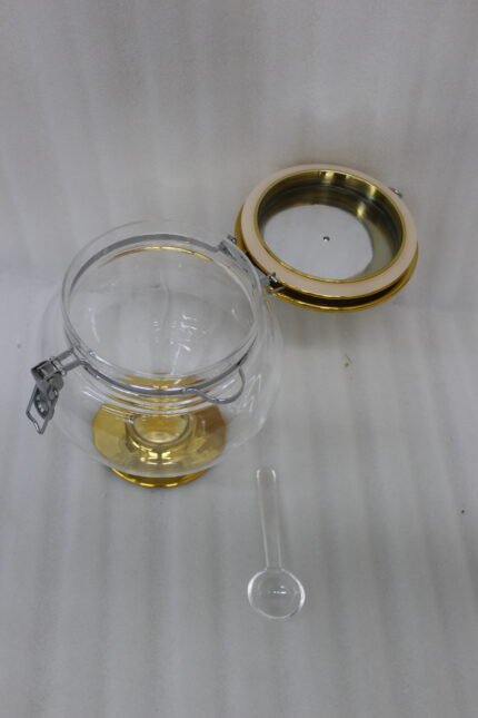 Three graduated clear acrylic jars with gold bases, lids, and matching spoons displayed on a dark countertop from One More Crockery.