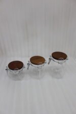 Three clear acrylic storage jars of varying sizes featuring wooden lids, airtight wire-clamp seals, and small hanging spoons, arranged on a white marble countertop in a modern kitchen.