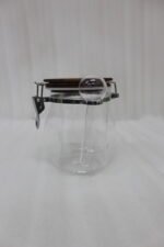 Clear acrylic kitchen storage jar set of three in varying sizes with wooden lids, airtight clasp locks, and attached spoons sitting on a dark marble countertop against a modern kitchen background.