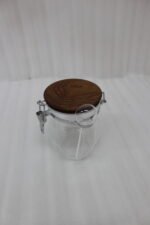 Clear acrylic kitchen storage jar set of three in varying sizes with wooden lids, airtight clasp locks, and attached spoons sitting on a dark marble countertop against a modern kitchen background.