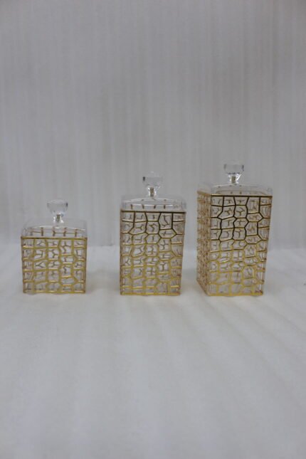 A luxury 3-piece clear acrylic jar set with gold geometric patterns and crystal lids, neatly arranged on a white marble kitchen countertop.
