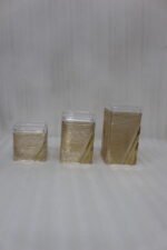 A set of three clear acrylic storage jars with decorative ribbed gold detailing, displayed neatly on a modern kitchen countertop.