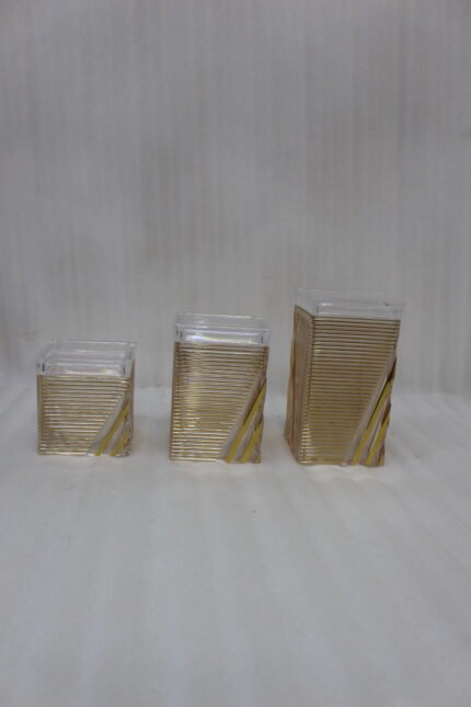 A set of three clear acrylic storage jars with decorative ribbed gold detailing, displayed neatly on a modern kitchen countertop.