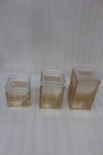 A set of three clear acrylic storage jars with decorative ribbed gold detailing, displayed neatly on a modern kitchen countertop.