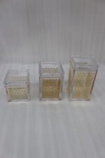 Set of three clear acrylic kitchen storage jars with elegant gold patterned designs, displayed on a marble countertop.