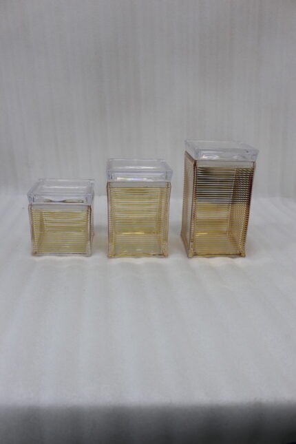 Three varying heights of clear ribbed acrylic storage jars with lids arranged on a modern kitchen countertop.