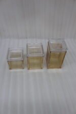 Three varying heights of clear ribbed acrylic storage jars with lids arranged on a modern kitchen countertop.