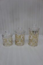 Three clear acrylic jars of varying heights featuring a gold floral print and clear lids, arranged on a marble kitchen countertop.