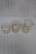 Three clear acrylic jars of varying heights featuring a gold floral print and clear lids, arranged on a marble kitchen countertop.