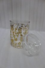 Three clear acrylic jars of varying heights featuring a gold floral print and clear lids, arranged on a marble kitchen countertop.