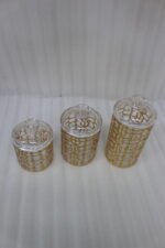 Three luxurious clear acrylic jars of varying heights featuring intricate gold geometric designs and matching lids, displayed neatly on a white marble countertop with a small golden spoon.