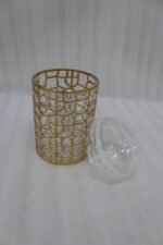 Three luxurious clear acrylic jars of varying heights featuring intricate gold geometric designs and matching lids, displayed neatly on a white marble countertop with a small golden spoon.