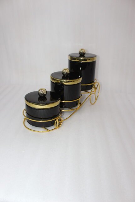 Luxury 3-piece black and gold ceramic storage jar set with golden lids arranged on an elegant gold metal cart stand on a modern kitchen countertop.