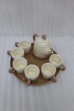 Beige and brown ceramic tea set with 6 cups, a teapot, and a rotating tray arranged on a kitchen counter