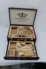 72-piece stainless steel cutlery set with gold trim handles and specialty serving utensils displayed on a white tray.