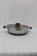 Four stainless steel double-handle woks with glass lids in 24cm, 26cm, 28cm, and 30cm sizes displayed on a dark kitchen countertop.