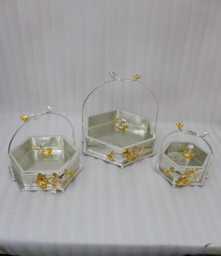 Three hexagonal silver and gold floral decorative serving dishes with handles resting on a wooden coffee table