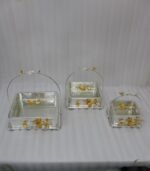 Three silver textured decorative serving dishes with gold floral accents and overhead arched handles on a wooden coffee table.