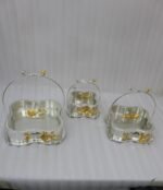 Three-piece silver hammered decorative bowl set with gold floral accents and overhead handles arranged on a wooden table.