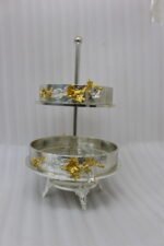 Two-tiered textured silver serving stand with gold floral accents displayed on a wooden table.