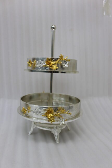 Two-tiered textured silver serving stand with gold floral accents displayed on a wooden table.