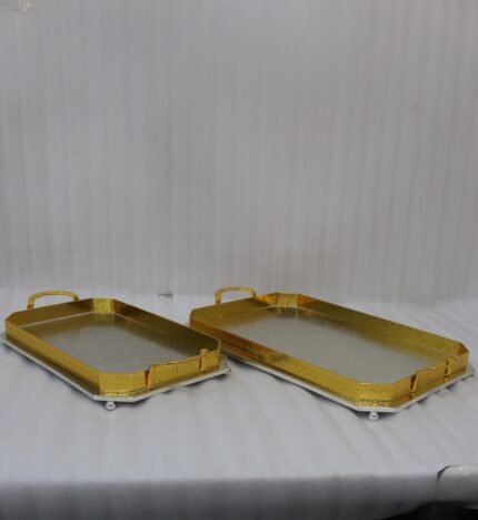 Set of two luxury gold and silver rectangular decorative serving trays with Greek key pattern borders resting on a white marble countertop.