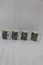 4-piece ceramic coffee mug set with black and grey geometric tribal patterns and gold rims lined up on a granite kitchen countertop