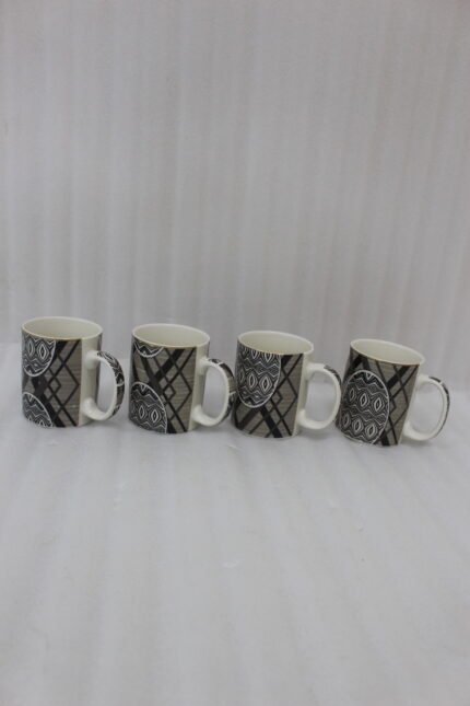 4-piece ceramic coffee mug set with black and grey geometric tribal patterns and gold rims lined up on a granite kitchen countertop