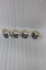 4-piece ceramic coffee mug set with black and grey geometric tribal patterns and gold rims lined up on a granite kitchen countertop