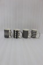 Four-piece modern black and white ceramic coffee mug set with geometric chevron and argyle patterns lined up on a kitchen counter.