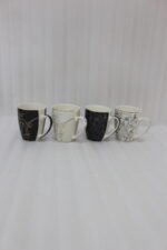 Set of 4 OneMore ceramic coffee mugs featuring abstract face line art in black, white, and gold on a kitchen countertop.