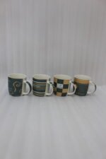 A row of four modern ceramic coffee mugs with black, cream, and brown coffee house patterns lined up on a white kitchen countertop.
