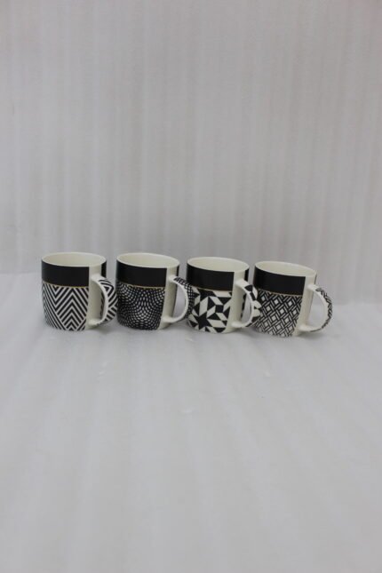 Set of four modern ceramic coffee mugs featuring black and white geometric patterns lined up on a granite countertop.