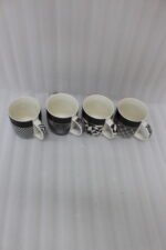 Set of four modern ceramic coffee mugs featuring black and white geometric patterns lined up on a granite countertop.