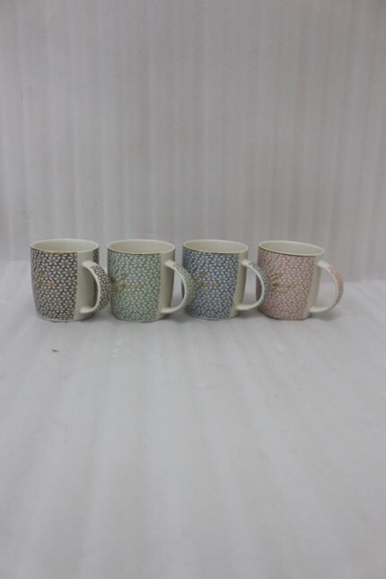 Four ceramic coffee mugs with pastel floral patterns in grey, green, blue, and pink featuring gold rims on a marble kitchen countertop.