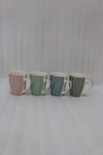 Four ceramic coffee mugs with pastel vertical stripes in pink, green, blue, and brown sitting on a marble kitchen countertop.