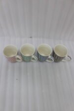 Four ceramic coffee mugs with pastel vertical stripes in pink, green, blue, and brown sitting on a marble kitchen countertop.