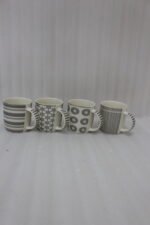 Set of 4 ceramic coffee mugs with charcoal grey geometric and striped patterns on a dark granite kitchen island counter.