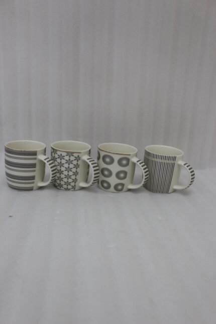 Set of 4 ceramic coffee mugs with charcoal grey geometric and striped patterns on a dark granite kitchen island counter.