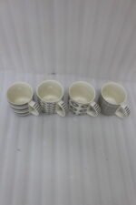 Set of 4 ceramic coffee mugs with charcoal grey geometric and striped patterns on a dark granite kitchen island counter.