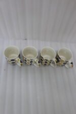 Set of four ceramic coffee mugs with mustard yellow and black geometric leaf prints displayed on a grey countertop.
