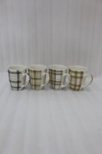 Set of four modern plaid ceramic coffee mugs displayed on a white marble kitchen countertop.