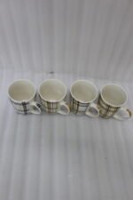 Set of four modern plaid ceramic coffee mugs displayed on a white marble kitchen countertop.
