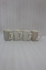 Set of four cream ceramic coffee mugs with metallic heart patterns and gold rims displayed on a marble kitchen countertop