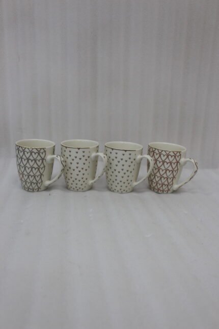 Set of four cream ceramic coffee mugs with metallic heart patterns and gold rims displayed on a marble kitchen countertop