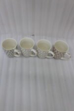 Set of four cream ceramic coffee mugs with metallic heart patterns and gold rims displayed on a marble kitchen countertop