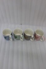 Four ceramic coffee mugs lined up on a kitchen counter in blue, green, brown, and pink with textured dot patterns and gold heart details.
