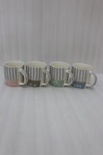 Four ceramic coffee mugs with black herringbone chevron patterns and colorful inspirational text labels lined up on a marble kitchen countertop.