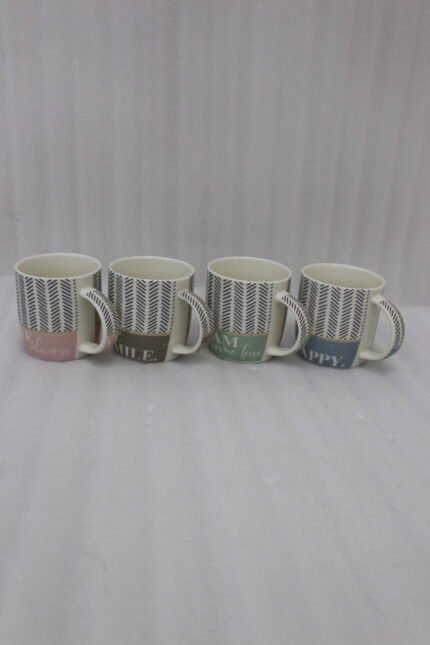 Four ceramic coffee mugs with black herringbone chevron patterns and colorful inspirational text labels lined up on a marble kitchen countertop.