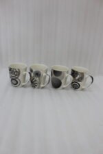 Set of 4 cream ceramic coffee mugs with distinct black geometric and swirl patterns displayed on a white marble countertop